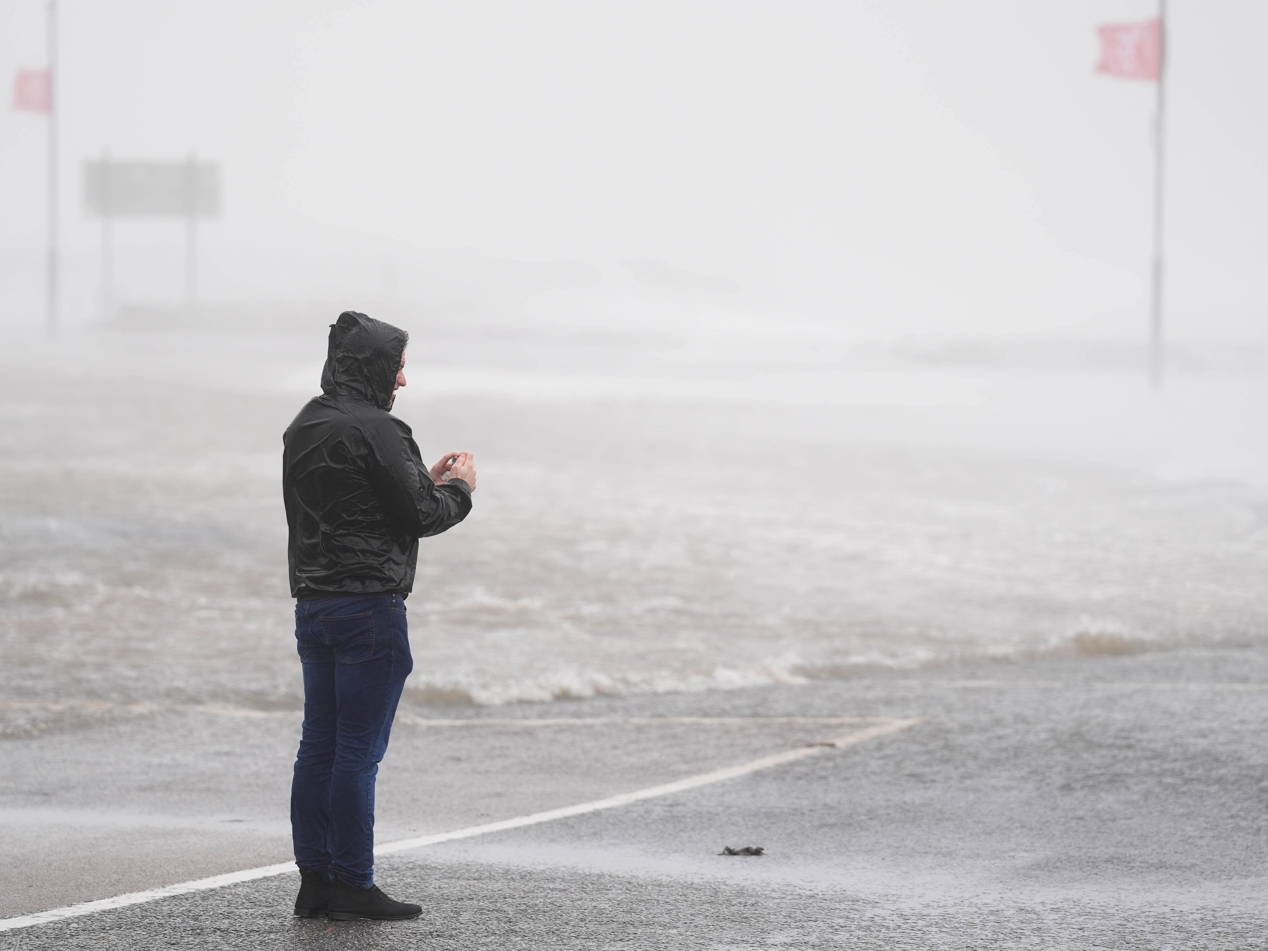 A man looks at a flooded road amid blustery weather